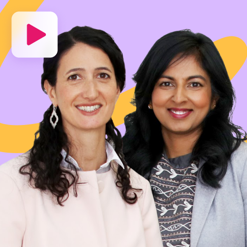 Two women, one with dark wavy hair and a light pink blazer, and the other with dark straight hair and a patterned top under a grey blazer, smile at the camera against a purple and orange background with a play button icon in the top left.